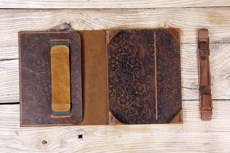 May include: A brown leather folio case with a floral embossed design. The case has a flap that closes with a snap and a handle on the side. The case is open to reveal a brown leather interior. A matching brown leather strap is included.