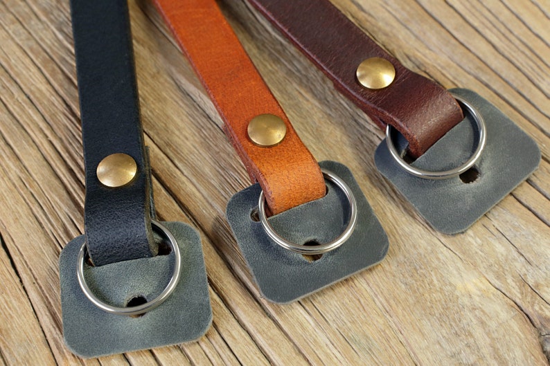 May include: Three leather camera straps with brass accents and metal rings. The straps are black, brown, and tan.