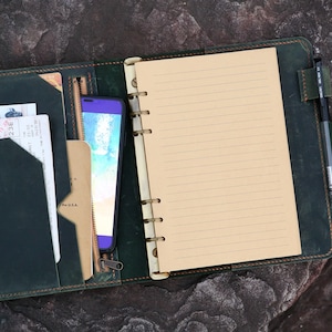 May include: A dark green leather bound journal with a zippered pocket, a phone, and a pen. The journal has a lined paper insert and a ring binder.