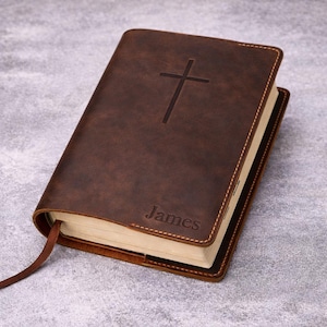 Może przedstawiać: Brązowa, skórzana książka z wytłoczonym krzyżem na okładce. Słowo "James" jest wytłoczone na dole. Książka ma szyte wiązanie i brązową wstążkę do zakładki.