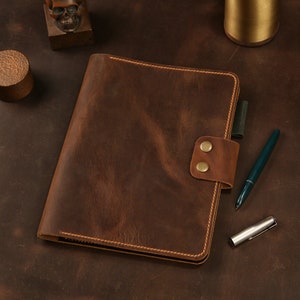 May include: A brown leather bound journal with a flap closure and two brass snaps. The journal has a distressed look and is stitched with brown thread.