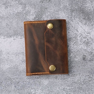 May include: A brown leather wallet with two brass snaps and a distressed look.