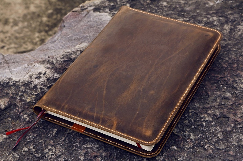 May include: A brown leather journal with a red ribbon bookmark. The journal has a distressed look and is stitched with a light brown thread.