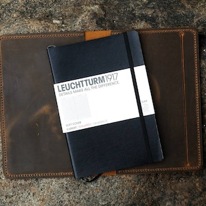 Puede incluir: Una cubierta de cuaderno de cuero marr&oacute;n con un cuaderno negro en el interior. El cuaderno tiene el texto "LEUCHTTURM1917" y "DETAILS MAKE ALL THE DIFFERENCE" en la portada.