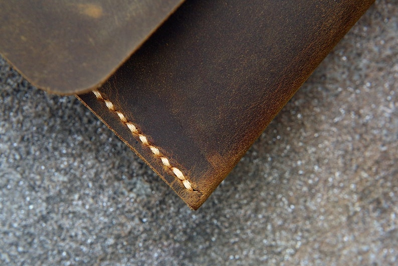 Op de afbeelding: Close-up van een bruine leren portemonnee met witte stiksels. De portemonnee is gemaakt van verweerd leer en heeft een rustieke uitstraling.