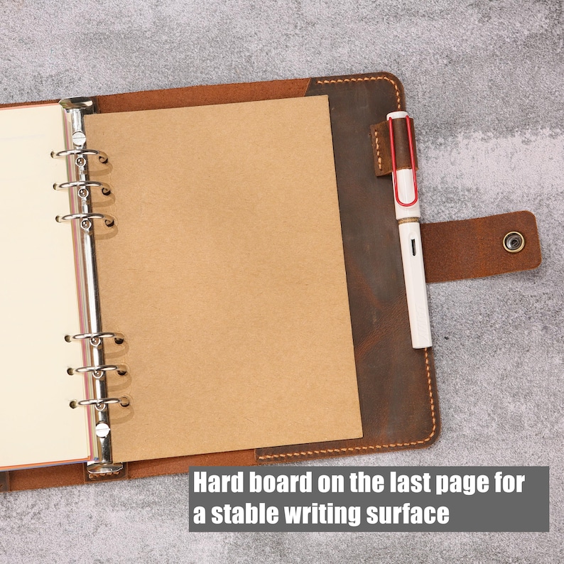 May include: A brown leather binder with a six-ring metal mechanism, containing cream-colored paper and a tan cardstock sheet. A white fountain pen with a red clip is held in a leather loop. Text reads: Hard board on the last page for a stable writing surface.