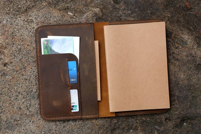 May include: A brown leather notebook cover with a built-in card holder and a blank notebook. The cover has a distressed look and is stitched with brown thread.