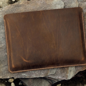 May include: A brown leather laptop sleeve with a stitched edge.