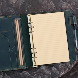 May include: A dark green leather bound journal with a zippered pocket and a pen holder. The journal has a lined paper insert and a ring binder.