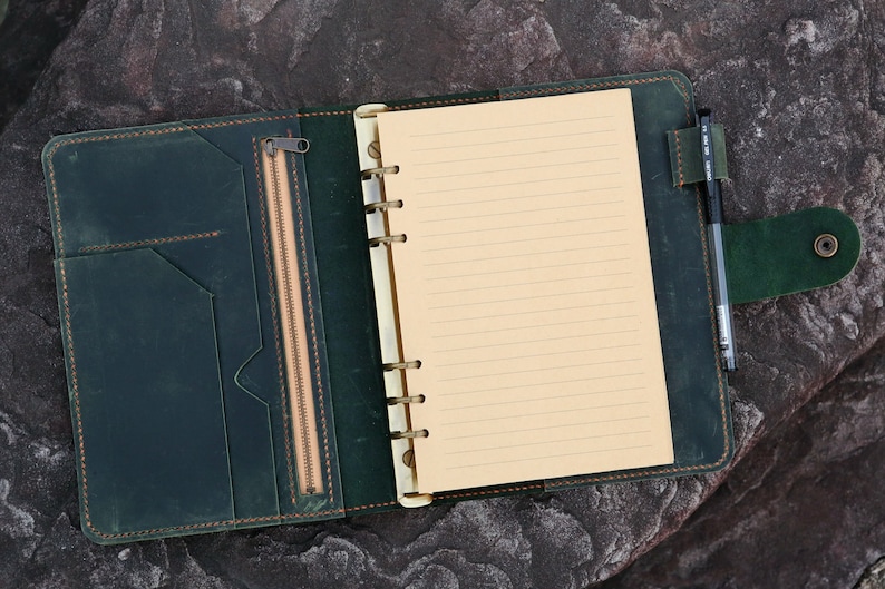 May include: A dark green leather bound journal with a zippered pocket and a pen holder. The journal has a lined paper insert and a ring binder.