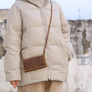 May include: A beige puffer jacket with a brown leather crossbody bag with an embossed floral design. The bag has a flap closure with a metal buckle.