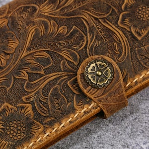 May include: A brown leather wallet with a floral embossed design. The wallet has a brass button closure.