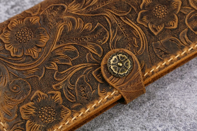 May include: A brown leather wallet with a floral embossed design. The wallet has a brass button closure.