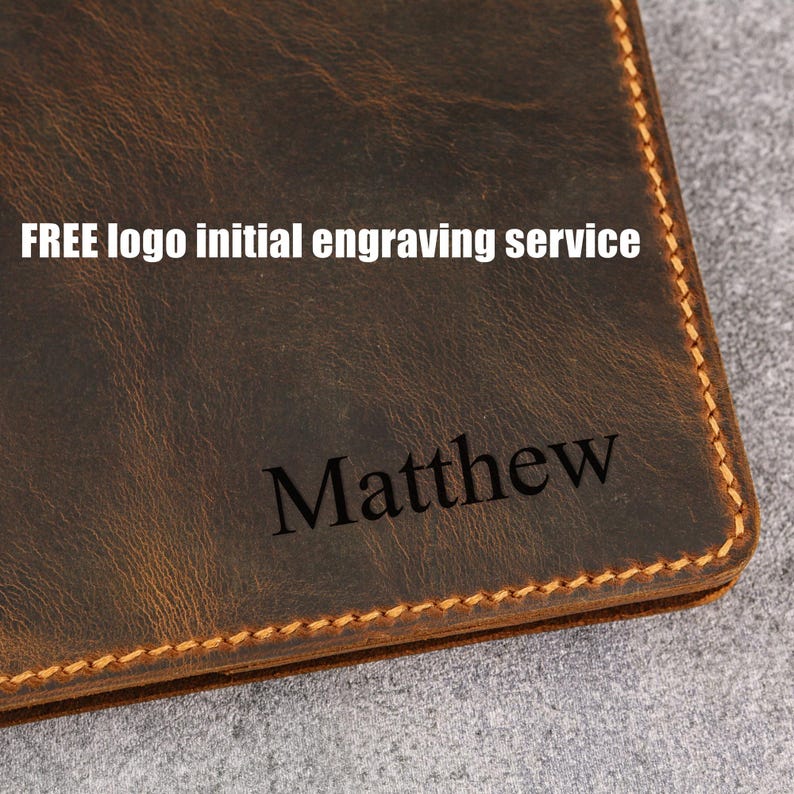 Op de afbeelding: Een donkerbruine lederen portemonnee met zichtbare stiksels langs de randen. Het oppervlak toont de gegraveerde naam Matthew en de gedrukte tekst FREE logo initial engraving service in een wit schreefloos lettertype op het leer.