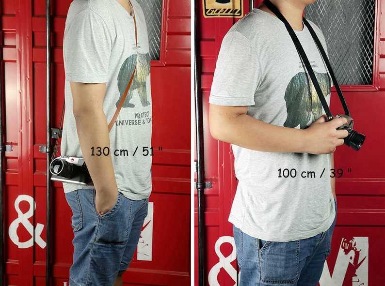 May include: Two people wearing gray t-shirts with a bear graphic and blue jeans are shown wearing camera straps. The strap on the left is brown leather and measures 51 inches long. The strap on the right is black and measures 39 inches long.  "Protect Universe & Today" is printed on the t-shirt.