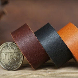 May include: Three leather straps in brown, black, and orange. The straps are rolled up and stacked on top of each other.
