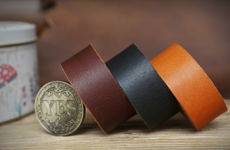 May include: Three leather straps in brown, black, and orange. The straps are rolled up and stacked on top of each other.