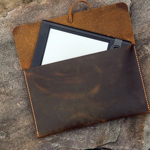 May include: A brown leather case with a flap that folds over to protect a tablet or e-reader. The case has a distressed look and is stitched with a light brown thread.