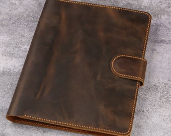 May include: A brown leather binder with a flap closure and a stitched edge. The binder has a distressed look and is made of high-quality leather.