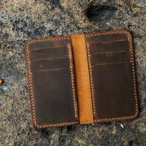May include: A brown leather wallet with multiple card slots and a brown leather flap. The wallet has a stitched edge and is closed.