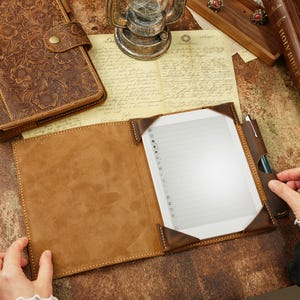 May include: A brown leather folio case with a flap closure and a built-in pen holder. The case is open to reveal a white e-reader with a blank screen.