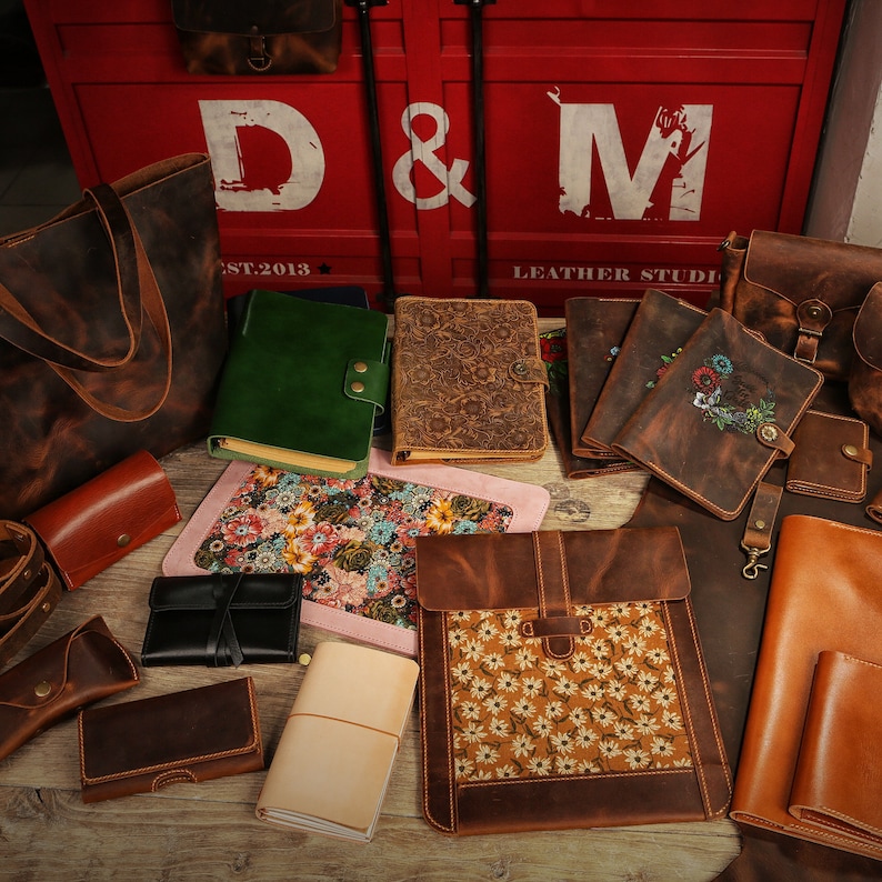 May include: A collection of leather goods, including totes, journals, and pouches, with floral patterns and the text "D&M Leather Studio" on a red background.