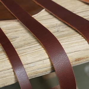 May include: Close-up of four brown leather straps laid out on a light wood surface. The straps are different widths and are arranged in a staggered pattern.