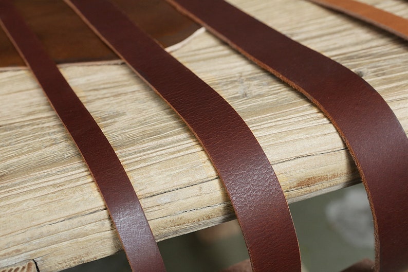 May include: Close-up of four brown leather straps laid out on a light wood surface. The straps are different widths and are arranged in a staggered pattern.