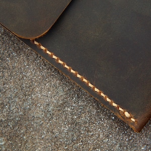 May include: Close-up of a dark brown leather wallet with a light brown stitching detail. The wallet is lying on a textured surface.