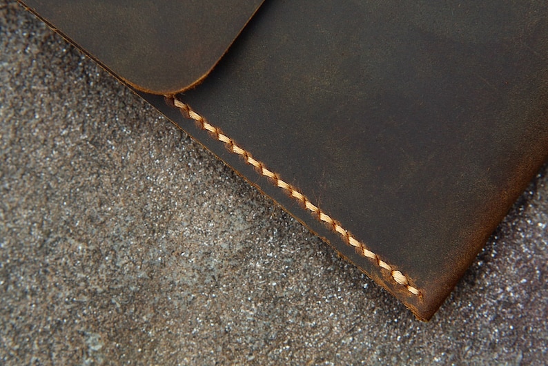 May include: Close-up of a dark brown leather wallet with a light brown stitching detail. The wallet is lying on a textured surface.