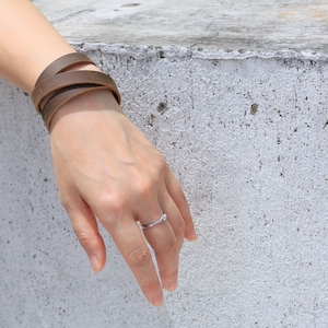 May include: A brown leather bracelet wrapped around a wrist. The bracelet is made of three strands of leather that are woven together.