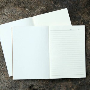 May include: An open notebook with lined pages on a textured brown surface. The notebook is white with a blank page on the left and lined pages on the right.