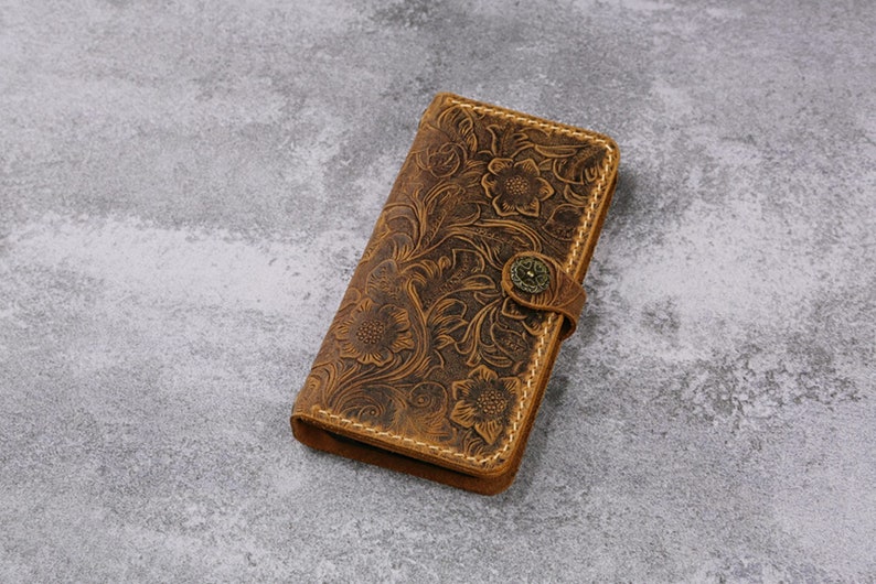 May include: A brown leather wallet with a floral embossed design and a brass button closure.