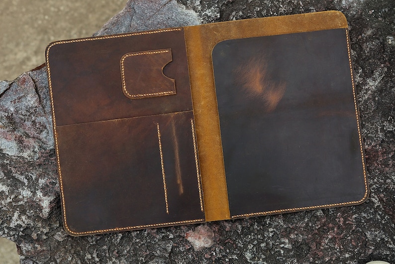 May include: A brown leather folder with a yellow leather interior. The folder has multiple pockets and a flap closure.