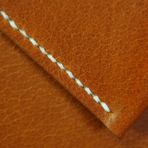 May include: Close-up of a brown leather surface with a white stitched seam. The leather has a textured, pebbled appearance.