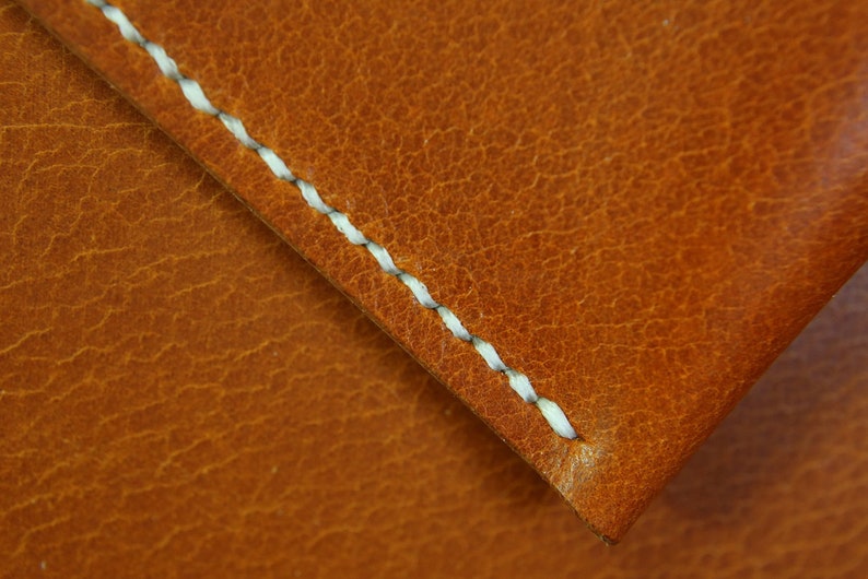 May include: Close-up of a brown leather surface with a white stitched seam. The leather has a textured, pebbled appearance.