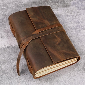 May include: A brown leather-bound journal with a flap closure and a leather strap. The journal has a distressed look and is closed.