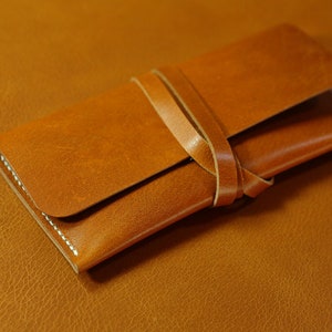 May include: A brown leather wallet with a strap closure. The wallet is folded in half and the strap is tied around it.