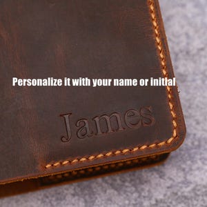 May include: Close-up of a brown leather wallet with the name "James" embossed on the front. The text "Personalize it with your name or initial" is above the name. The edges are stitched with a contrasting thread.
