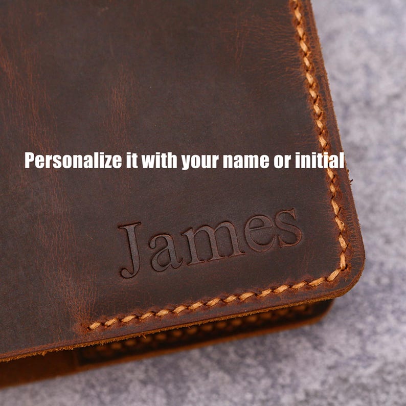 May include: Close-up of a brown leather wallet with the name "James" embossed on the front. The text "Personalize it with your name or initial" is above the name. The edges are stitched with a contrasting thread.