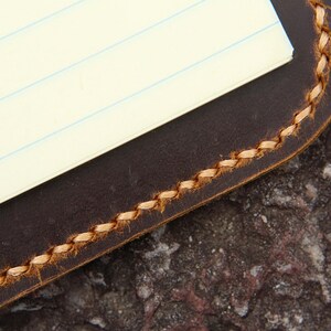 May include: A brown leather notebook cover with a stitched edge and a lined paper insert.