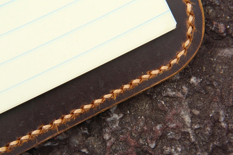May include: A brown leather notebook cover with a stitched edge and a lined paper insert.