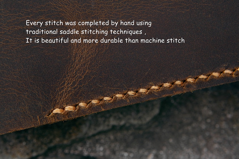 Op de afbeelding: Close-up van bruin leer met handgestikte details. De beige draad cre&euml;ert een contrasterend patroon. Tekst luidt: "Elke steek is met de hand voltooid met behulp van traditionele zadelstitchingstechnieken." Het leer heeft een verweerde uitstraling.
