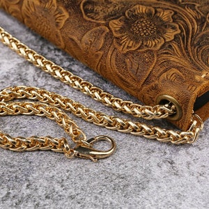 May include: A brown leather phone case with a floral embossed design and a gold chain strap.