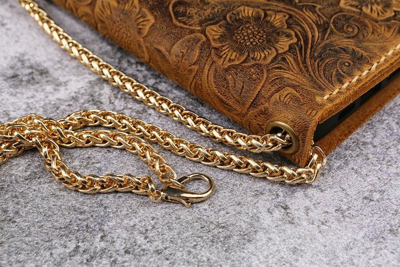 May include: A brown leather phone case with a floral embossed design and a gold chain strap.