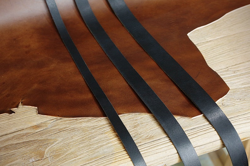 May include: Three black leather straps laid out on a brown leather surface. The straps are different widths and lengths.