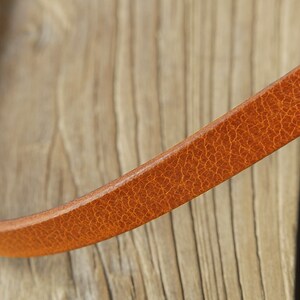 May include: Close-up of a brown leather strap with a textured surface.