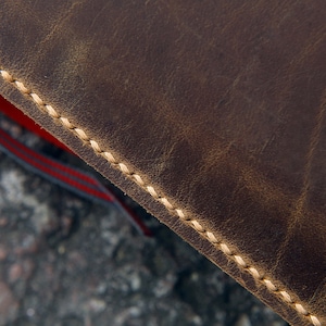May include: Close-up of brown leather with a stitched edge. The stitching is a light beige color.