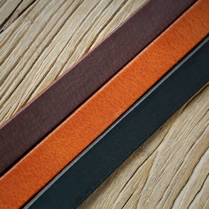 May include: Three leather straps in different colors: dark brown, orange, and black. The straps are laid out on a wooden surface.