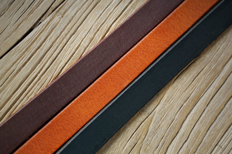 May include: Three leather straps in different colors: dark brown, orange, and black. The straps are laid out on a wooden surface.